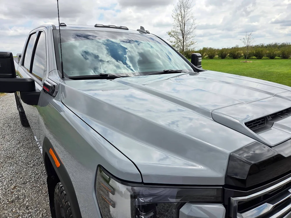 Silver RAM HD truck hood detailed, parked by farm equipment